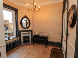 An entryway with a wooden floor a black table a fireplace and a round mirror at Coronation House in Scarborough