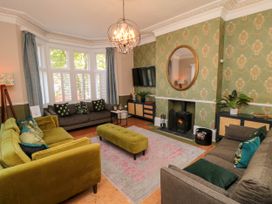 A living room with green and gray sofas a green ottoman a wall-mounted TV and a fireplace at Coronation House in Scarborough