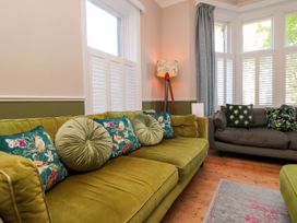A living room with green and gray sofas a standing lamp wooden floor and windows with shutters and curtains at Coronation House in Scarborough