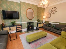 A living room with green patterned wallpaper a fireplace two sofas a green ottoman and a wall mounted tv at Coronation House in Scarborough