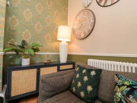 A corner of a living room with a sofa a sideboard with a lamp and plant and a wall clock at Coronation House in Scarborough
