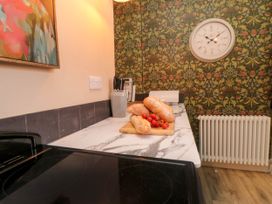 A kitchen countertop with bread and tomatoes on a cutting board a knife block a toaster a wall clock a radiator and floral patterned wallpaper at Coronation House in Scarborough