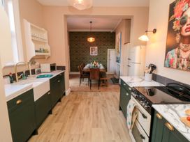 A kitchen with green cabinets a white farmhouse sink a stove and a refrigerator leading to a dining area with a long table and chairs at Coronation House in Scarborough