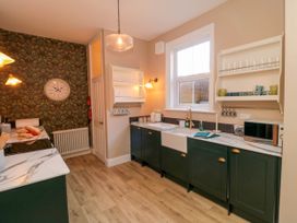 A kitchen with dark green cabinets white marble countertops open shelves cups and glasses a clock on wallpapered wall at Coronation House in Scarborough
