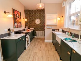 A kitchen with dark green cabinets white countertops a stove a sink a large window and patterned wallpaper at Coronation House in Scarborough