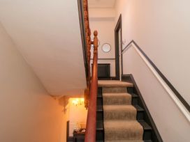 A staircase with beige carpet runner and wooden banister leading to a hallway with a black radiator and round mirror at Coronation House in Scarborough