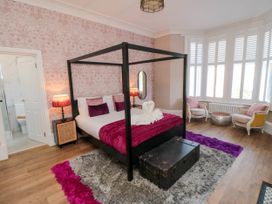 A bedroom with a four-poster bed two armchairs a trunk and large windows at Coronation House in Scarborough