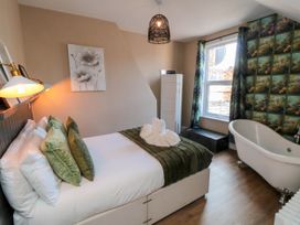 A bedroom with a bed, green pillows, a freestanding bathtub, a window with curtains, and a decorative wall at Coronation House in Scarborough