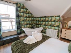 A bedroom with a white freestanding bathtub floral wallpaper bed with green cover and towel swans at Coronation House in Scarborough