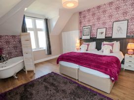 A bedroom with two single beds joined together a purple blanket a bathtub and floral wallpaper at Coronation House in Scarborough