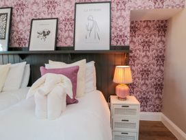 A bedroom with two beds a bedside table with a lamp and framed artwork on a pink floral wallpaper at Coronation House in Scarborough