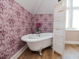 A bathroom with a clawfoot bathtub floral wallpaper wooden floor and a folding privacy screen at Coronation House in Scarborough