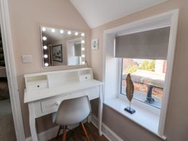 A white dressing table with lighted mirror and chair next to a window with a decorative feather at Coronation House in Scarborough