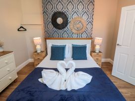A bedroom with a bed decorated with towel swans blue pillows bedside tables with lamps and patterned wallpaper at Coronation House in Scarborough