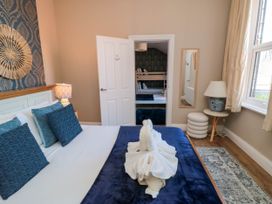 A bedroom with a bed and blue pillows next to a bedside lamp and an open door showing another room with bunk beds at Coronation House Scarborough