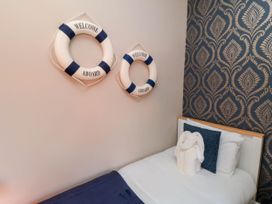A bedroom with a single bed white and blue bedding two life rings on the wall and patterned wallpaper at Coronation House Scarborough