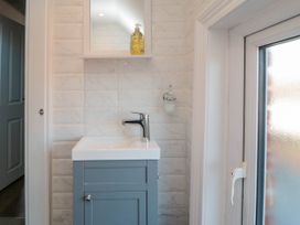 A bathroom sink with a faucet and cabinet below a wall mirror with a soap dispenser beside a frosted window at Coronation House in Scarborough