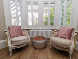 Two armchairs with pink cushions and a round metallic table in front of a window with white shutters at Coronation House in Scarborough