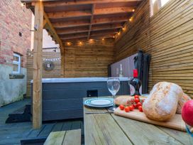 An outdoor covered patio area with a wooden table set up with bread cherry tomatoes and glasses near a hot tub at Coronation House in Scarborough