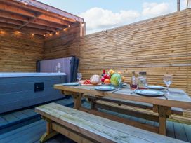 An outdoor wooden dining table with plates glasses fruit bread and bottles next to a hot tub in a fenced patio at Coronation House in Scarborough