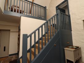 Staircase with blue-gray railing and brown carpet next to small white cabinet with tray at The Old Coach House in Eglingham near Alnwick