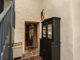 A hallway with a black cabinet holding dishes a small table and staircase railing at The Old Coach House in Eglingham near Alnwick