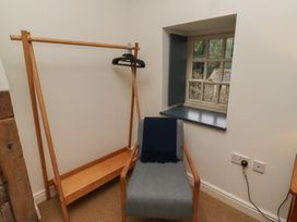 A corner with a wooden clothes rack with hangers and a grey chair with a dark cloth in front of a window at The Old Coach House Eglingham near Alnwick
