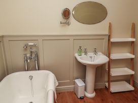 A bathroom with a bathtub a sink a mirror a soap dispenser a waste bin and a wooden shelving unit at The Old Coach House in Eglingham near Alnwick