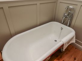 A clawfoot bathtub with towel hanging on the side and vintage faucet on wooden floor at The Old Coach House in Eglingham near Alnwick