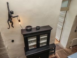 A black cabinet with glass doors and bowls on top under a monkey-shaped wall lamp holding a light bulb in a room with stone floor at The Old Coach House in Eglingham near Alnwick