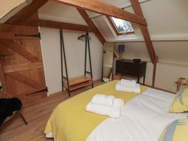 A bedroom with a bed with yellow and white bedding towels on the bed a wooden door a clothes rack a mirror a small dark wooden dresser and a skylight window at The Old Coach House Eglingham near Alnwick