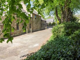 A stone building beside a paved road with trees and bushes at The Old Coach House in Eglingham near Alnwick