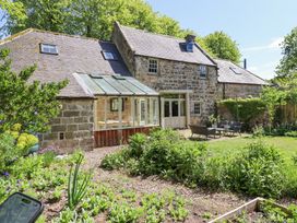A stone house with a glass conservatory and garden furniture in a garden with plants and trees at The Old Coach House in Eglingham near Alnwick