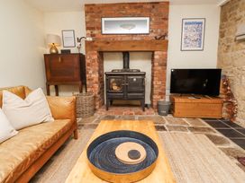 A living room with a leather sofa a wood burning stove and a television on a wooden chest at The Old Coach House in Eglingham near Alnwick