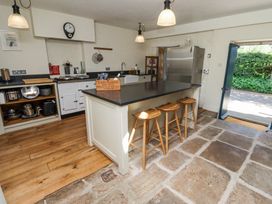 A kitchen with a large island and three stools a refrigerator and an open door showing greenery outside at The Old Coach House Eglingham near Alnwick