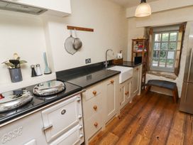 A kitchen with a white stove black countertops a farmhouse sink a wooden floor and a window with a small shelf and stool at The Old Coach House in Eglingham near Alnwick