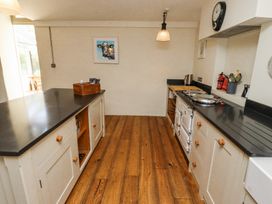 A kitchen with wooden floor cabinets a stove and a cow picture on the wall at The Old Coach House in Eglingham near Alnwick