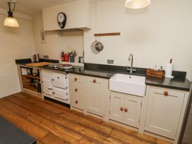 A kitchen with a white stove a sink and cabinets on a wooden floor at The Old Coach House in Eglingham near Alnwick