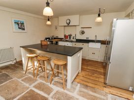 A kitchen with an island and three wooden stools a refrigerator and a sink at The Old Coach House in Eglingham near Alnwick