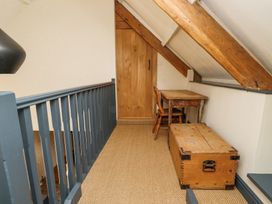 A narrow loft space with a wooden door a wooden chair a small wooden table a wooden chest and a blue railing at The Old Coach House in Eglingham near Alnwick