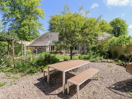 An outdoor garden with a wooden picnic table and benches on gravel near a stone house at The Old Coach House in Eglingham near Alnwick