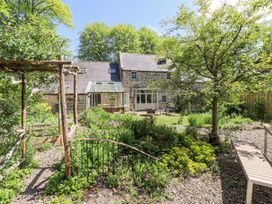 A garden with plants trees a wooden pergola and a stone house in the background at The Old Coach House in Eglingham near Alnwick