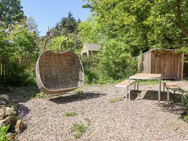 A garden area with a wicker hanging chair a table with two benches a shed and trees at The Old Coach House in Eglingham near Alnwick