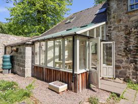 An exterior view of a stone house with a glass sunroom and open double doors at The Old Coach House in Eglingham near Alnwick