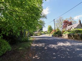 A paved road lined with trees and houses under a blue sky at The Old Coach House in Eglingham near Alnwick