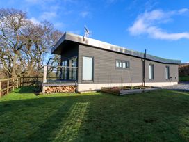 A modern single-story house with a glass balcony and wood storage under the deck in a grassy yard with trees at Dundarach in Aberfeldy