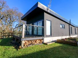 A modern house with glass balcony and stacked firewood under the deck surrounded by grass and trees at Dundarach in Aberfeldy