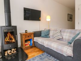 A living room with a wood burning stove a wooden side table and a sofa with cushions at Dundarach Aberfeldy