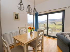 A dining area with a wooden table and four chairs next to large glass sliding doors showing a balcony and a mountain view at Dundarach in Aberfeldy