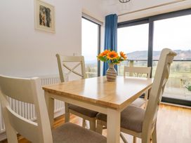 A dining table with four chairs and a vase with flowers near a large window with blue curtains at Dundarach in Aberfeldy